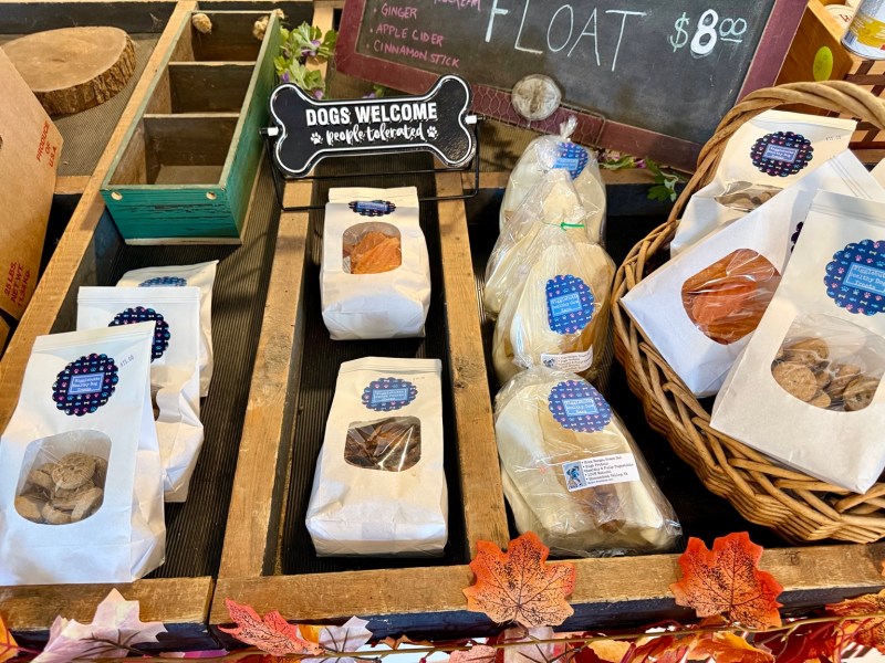 Locally made dog treats beside a sign welcoming dogs to the orchard.