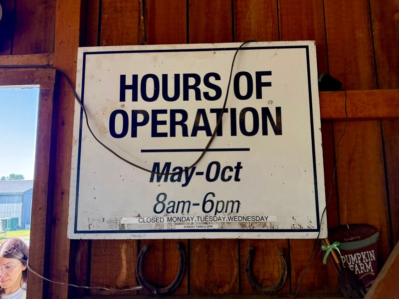 A rustic sign displaying the farm’s seasonal hours of operation.
