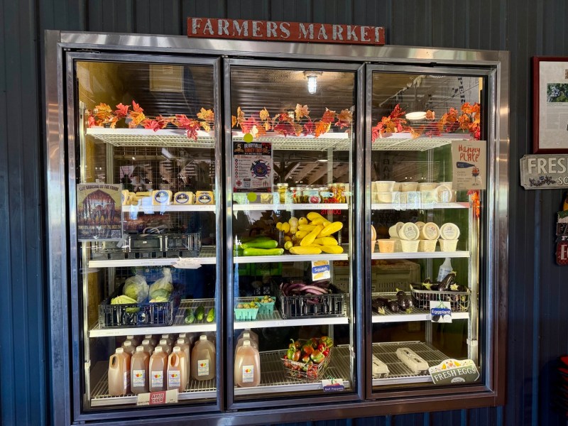 A refrigerated market case stocked with local produce, drinks and prepared goods.