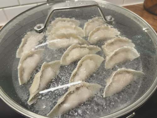 Homemade dumplings cooking in a covered pan.